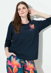 Marineblaues Langarmoberteil mit einem Blumenmotiv in Pink und Orange, kombiniert mit bunten Hosen mit großem Blumenmuster.