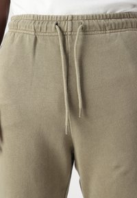 Lysebrune joggebukser laget av myk, strukturert stoff. Har elastisk midje med snor og sidelommer.