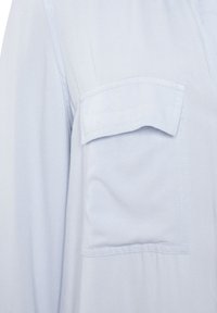 Light blue fabric shirt featuring a single chest pocket, soft texture, and a relaxed fit. Details include neat stitching along seams.