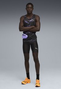 Puma atletisk tanktop i sort med lilla accenter, sorte kompressionsshorts og klare orange løbesko. Inkluderer også en lilla talje taske.