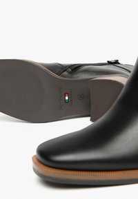 Schwarze Leder-Ankle-Boots mit glatter Oberfläche, seitlichem Reißverschluss und einer robusten braunen Sohle mit subtilen strukturierten Details.