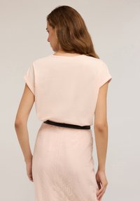 Ljusrosa, kortärmad topp med upprullade ärmar, kombinerad med en texturerad rosa kjol med spetsdetaljer och ett svart midjeband.