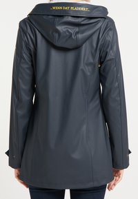 Veste imperméable bleu marine avec une finition brillante, capuche ajustable et texte doré sur le col. Présente une coupe ajustée et des boutons-pression en accent.