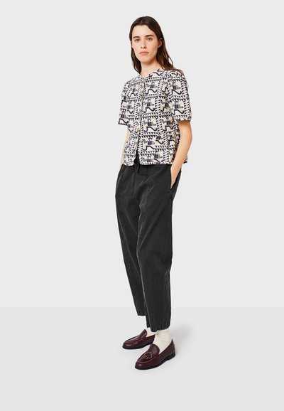 Camicia a maniche corte con bottoni, con un motivo geometrico blu navy e crema, abbinata a pantaloni larghi neri e mocassini bordeaux.