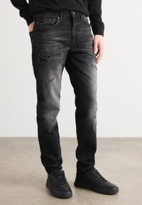 Jeans negri estompați cu un design uzat, având buzunare cu accesorii metalice, croială slim și un material neted, ușor texturat.