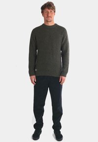 Suéter de canalé verde oscuro con cuello redondo, acabado texturizado y mangas largas, combinado con pantalones oscuros y zapatos negros.