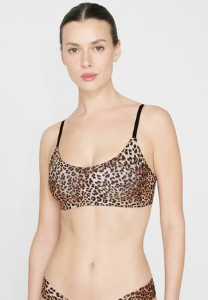 Vrouw draagt een leopardprint bralette met zwarte bandjes en bijpassend leopardprint ondergoed tegen een witte achtergrond.