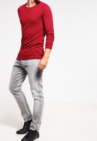 Pull rouge ajusté à manches longues avec un col rond, associé à un jean slim gris clair et des baskets noires. Design simple, sans motifs.
