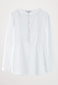 Valkoinen pitkähihainen paita, jossa on pyöreä kaula-aukko, edessä napitus, rypytys vyötäröllä ja pieni logo-yksityiskohta helman kohdalla.