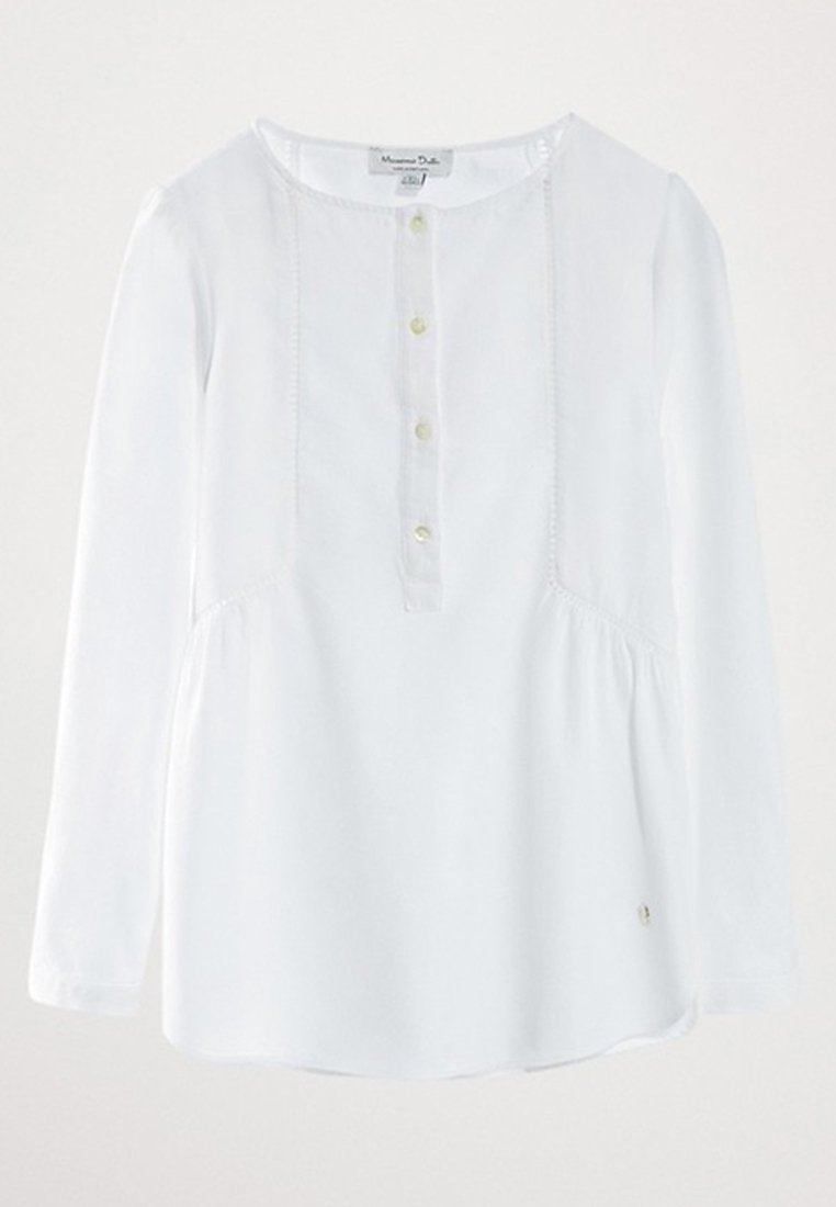 Valkoinen pitkähihainen paita, jossa on pyöreä kaula-aukko, edessä napitus, rypytys vyötäröllä ja pieni logo-yksityiskohta helman kohdalla.