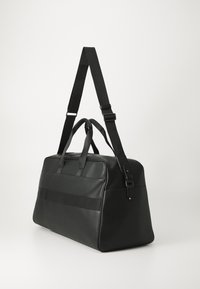 Black polymer travel bag with a rectangular shape, double handles, adjustable strap, and horizontal accent bands on the front.