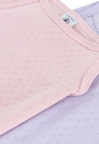 Zwei weiche, leichte ärmellose Oberteile in Pink und Flieder, ausgestattet mit einem strukturierten Stoff mit kleinen gemusterten Löchern und gewellten Kanten.
