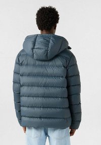 Chaqueta acolchada azul marino con capucha, con un diseño acolchado y secciones horizontales. Textura suave y brillante; botones y cierre de cremallera visibles.