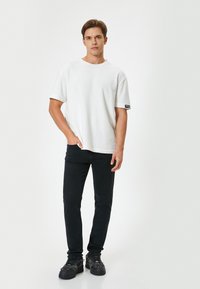 T-shirt bianca a maniche corte con scollatura rotonda, indossata con jeans neri slim-fit e sneakers nere con un design testurizzato.