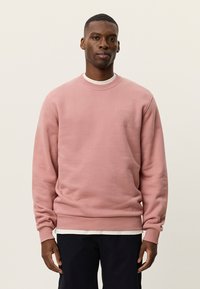 Ροζ φούτερ από μαλακό ύφασμα, με στρογγυλή λαιμόκοψη, ριμπ μανσέτες και διακριτικό λογότυπο στο αριστερό μέρος του στήθους.