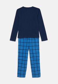 Haut à manches longues bleu marine avec un col rond, associé à un pantalon à carreaux bleu et noir, offrant une texture en coton doux.