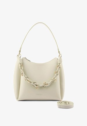 Bolso de mano color crema con asa trenzada decorada con anillos dorados, cierre de cremallera y correa de hombro desmontable colocada a su lado.