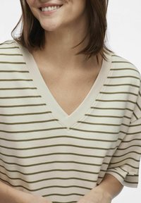 Krótki rękaw bluzka w odcieniu kremowym w oliwkowe paski. Posiada luźny krój i gładką teksturę tkaniny.