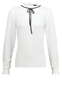 Blouse blanche à manches longues avec col et poignets volantés, ornée d'un nœud papillon noir au niveau du cou et d'une finition en tissu texturé.