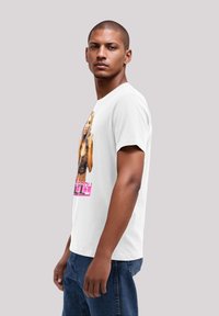 Weißes T-Shirt mit einem grafischen Druck einer Frau mit langen Haaren, die ein schwarzes Oberteil trägt. Der Druck zeigt den Namen "Britney" in pinkem Text.