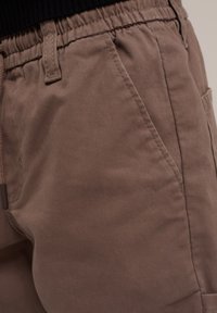 Pantalones de algodón marrón con cinturilla elástica, bolsillos laterales y una textura suave, que muestran detalles de costura sutiles.