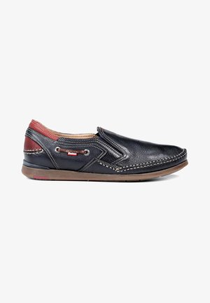 Chaussure noire en cuir à enfiler avec des accents rouges, des coutures décoratives, une semelle en caoutchouc marron et des œillets sur le côté pour la ventilation.