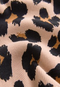 Tissu imprimé léopard avec une texture côtelée. Présente de grandes taches noires sur une base beige clair avec des accents marron, mettant en valeur un matériau doux et flexible.