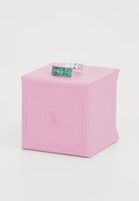 Zwei Ringe auf einer rosa, sechseckigen Box: der eine verfügt über grüne rechteckige Steine, der andere hat runde klare Steine, beide in silberfarbenem Metall gefasst.