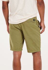 Olivgrüne Shorts aus Baumwolle, mit seitlichen und hinteren Taschen, entspannter Passform und genähtem Saum. Einfaches, funktionales Design.