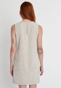 Beige Cordkleid mit strukturiertem Oberflächen, ärmellosem Design und einem Rückenschlitz. Gerade Silhouette mit einem Saum oberhalb des Knies.