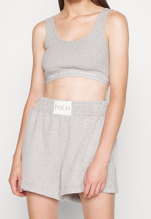 Nainen, joka pukeutuu vaaleanharmaaseen ribbineulottuun lyhyeen toppiin ja siihen sopiviin elastiseen vyötäröön leikattuihin shortseihin, molemmat Polo Ralph Lauren -merkittyjä, seisoo valkoista taustaa vasten.