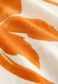 Audums ar dzelteno-oranžu botānisko rakstu uz balta fona. Audumam ir teksturēta, pinuma izskata virsma, kas izceļ ziedu dizainu.