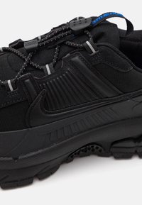 Scarpa da ginnastica nera Nike con suola testurizzata, pannello laterale a costine, asole riflettenti per i lacci e linguetta con dettaglio blu.