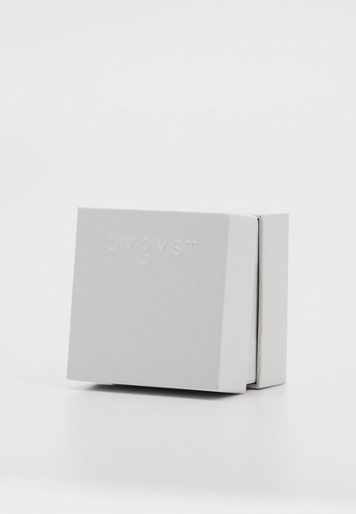 Kvadratisk, matt vit förpackning med präglad text "avgvst." Texturerad yta, inga synliga stängningar. Ren, minimalistisk design.