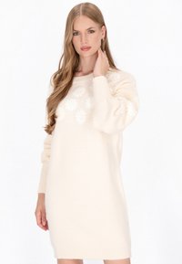 Cremefarvet strikket sweaterkjole med blomsterbroderi foran, teksturerede ærmer og ribbede manchetter. Blødt og oversized fit.