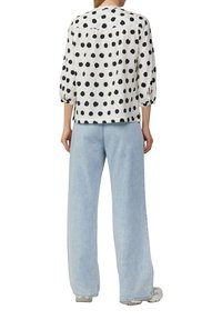 Witte top met zwarte stippen, losse pasvorm, driekwart pofmouwen. Gecombineerd met lichtblauwe wijde jeans en grijze sneakers.
