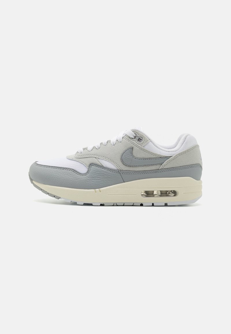 Nike Air Max 1 sneaker fehér és világosszürke színben, bőr és hálós felsőrészével, kerek orrával, párnázott gallérjával és látható légpárnájával.