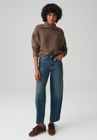 Brown ribbed knit sweater with a collar, paired with high-waisted blue jeans and brown suede sneakers. Simple design, relaxed fit.