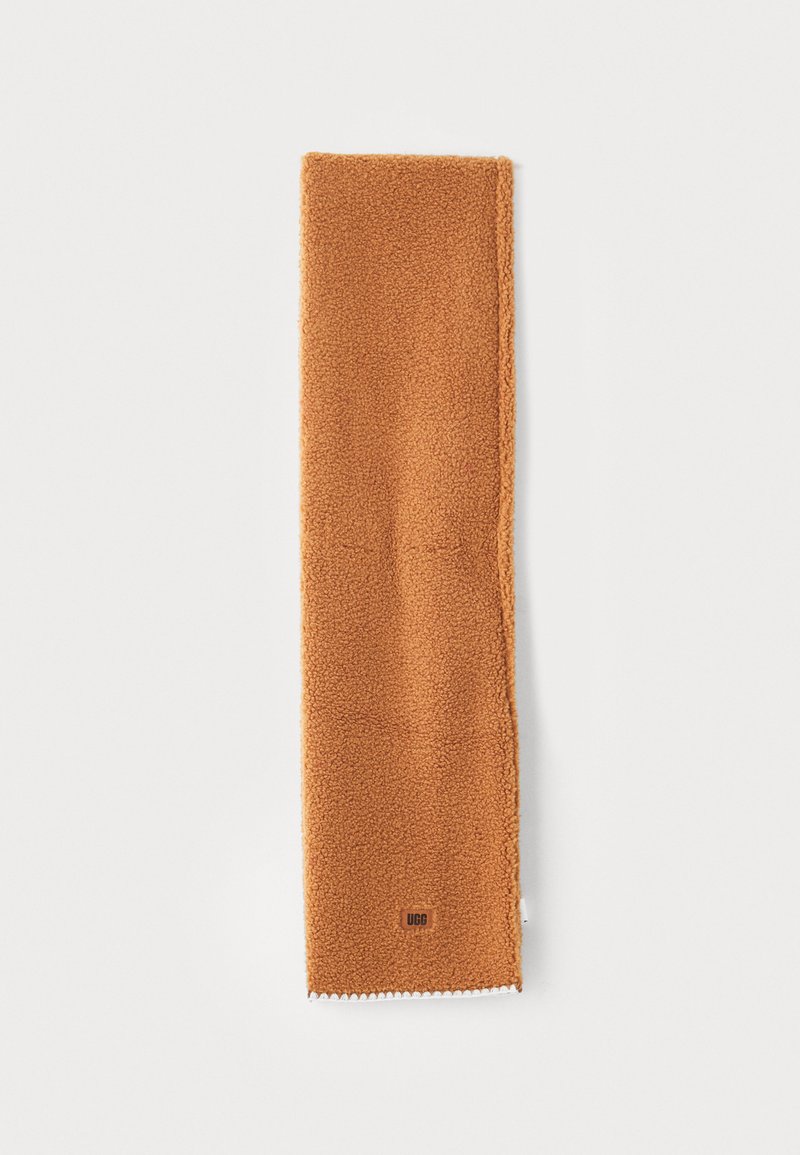 Brown fleece scarf with a soft texture, featuring stitched edges and a small logo label at the bottom. Long and rectangular shape.