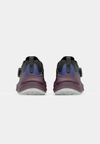 Black and purple athletic shoes with a textured upper, rear pull tab, and a chunky lavender sole. Features a circular hardware adjustment.