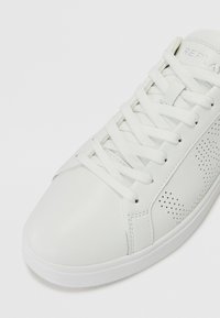 Weiße Ledersneaker mit glatter Oberfläche, perforierten Akzenten, runder Zehenpartie und flachen weißen Schnürsenkeln. Texturierte Sohle für besseren Halt.