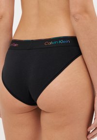 Črne bombažne bikini hlačke z barvitim logotipom Calvin Klein na pasu. Gladka tekstura in standardni kroj na zadnji strani.