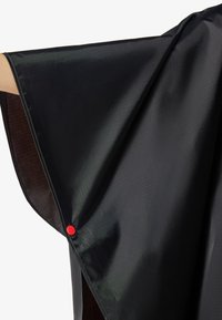 Μαύρο αδιάβροχο πόνοτσο με υφή και εμφανές κόκκινο κουμπί τύπου στερέωσης στη μια πλευρά, κοντά σε τεντωμένο χέρι.