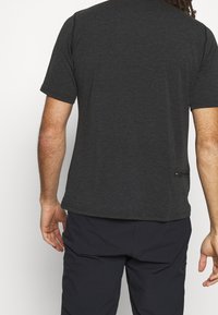 Mörkgrå kortärmad skjorta med en slät yta, med rundad nederkant och en liten märkt etikett i nedre vänstra delen av ryggen.