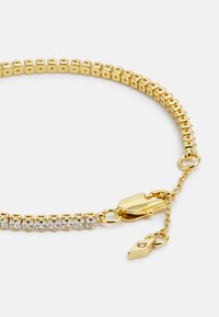 Guldring med et fleksibelt design og små rektangulære led. Accentueret med klare rhinsten og en solid lobster clasp lukning.