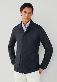 Chaqueta ligera de color azul marino, con una textura suave, que presenta un cuello con solapas, dos bolsillos frontales y un diseño elegante. Ideal para superponer.