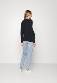 Sweater preto com nervuras e mangas longas, com uma silhueta ajustada, combinado com jeans de corte solto azul claro e ténis brancos, visto de costas.