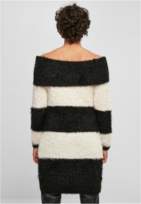 Pull oversize à épaules dénudées avec des rayures horizontales noires et crème. Fabriqué en matière texturée et duveteuse. Manches longues et coupe mi-longue.