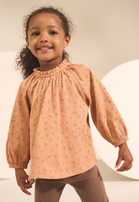 Haut à manches longues couleur pêche avec petits motifs floraux, encolure froncée et tissu texturé ; coupe ample avec poignets élastiques.