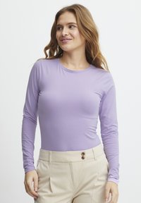 Paarse top met lange mouwen van een gladde, rekbare stof. Ronde halslijn en een getailleerd ontwerp, gecombineerd met beige hoge taillebroeken met knoopaccenten.